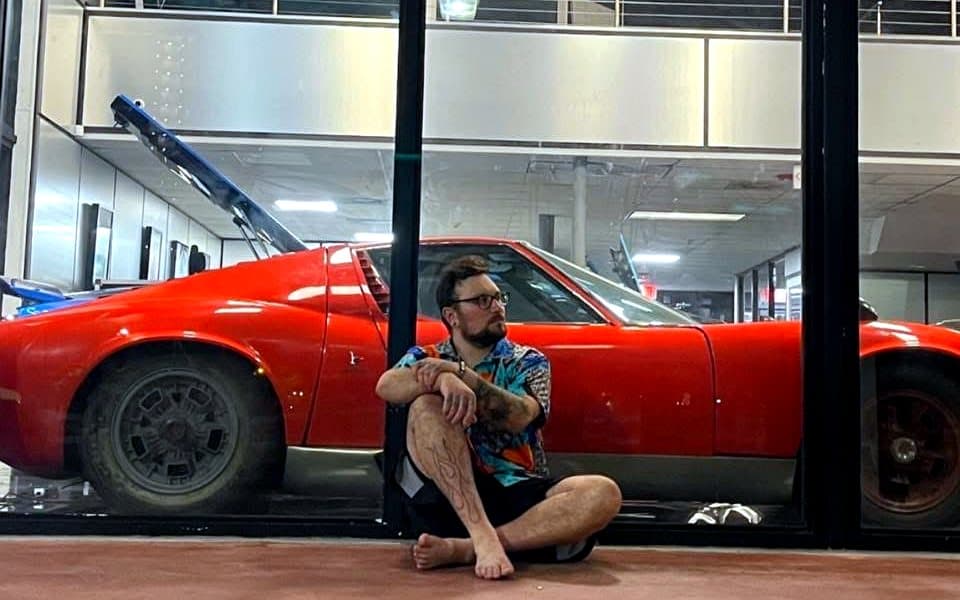 Sam assis devant une Lamborghini Miura classique rouge